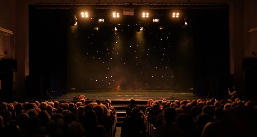 A brightly lit stage with performers, while an engaged audience watches from their seats