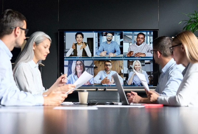 A diverse group of professionals in a conference room participating in a video conference with remote attendees