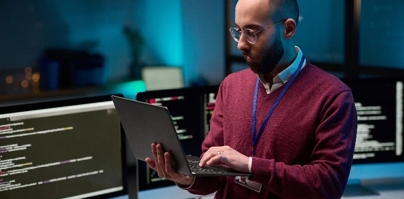 A man in a sweater is focused on a laptop screen