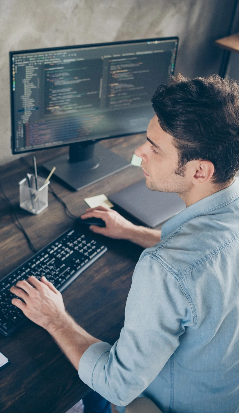 A man sits at a desk focused on a computer with a keyboard in front of him