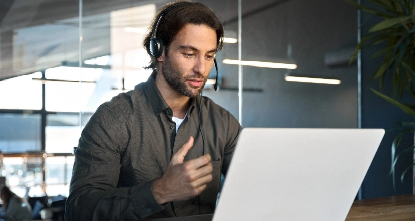 A man with headphones and a headset is focused on working on his laptop