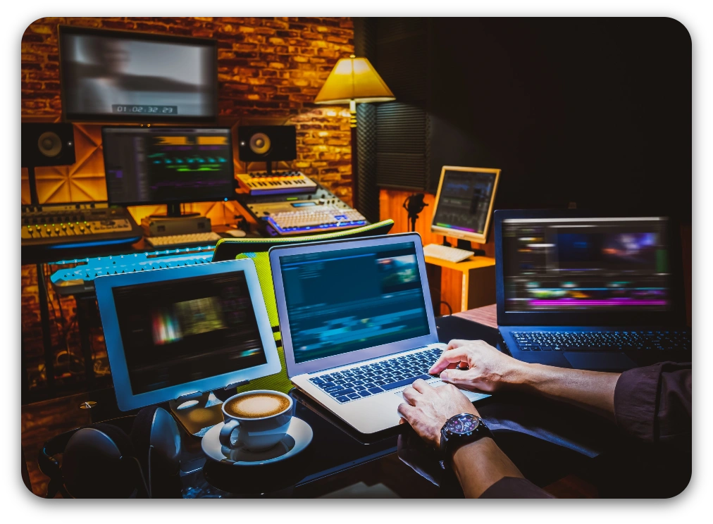 A person focused on a laptop while surrounded by recording equipment in a professional studio setting