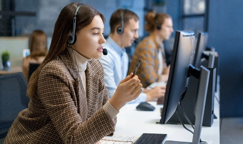 A woman wearing headphones, focused on her work in a busy call center environment.
