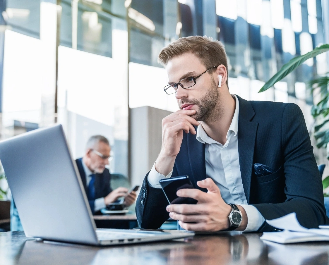 A young businessman thoughtfully examines his phone in a modern office setting