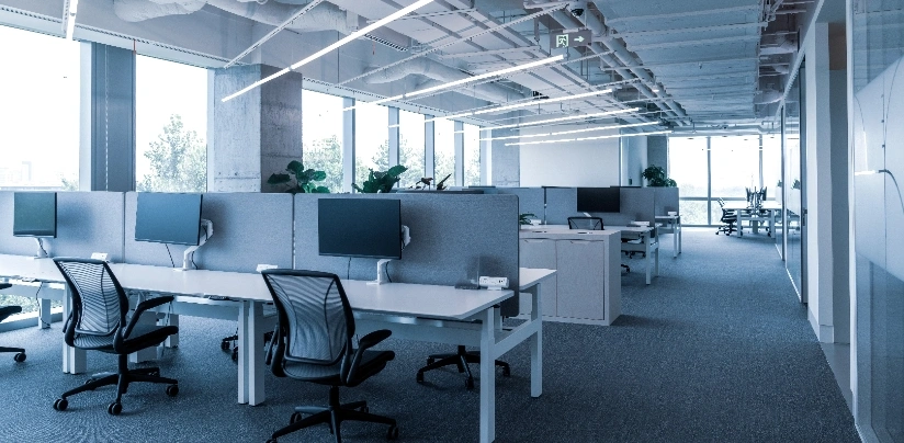 An office space featuring desks and chairs arranged in front of large windows