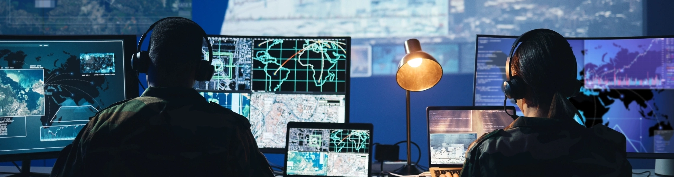 Two people collaborating at a desk with multiple computer monitors displaying various data and graphics