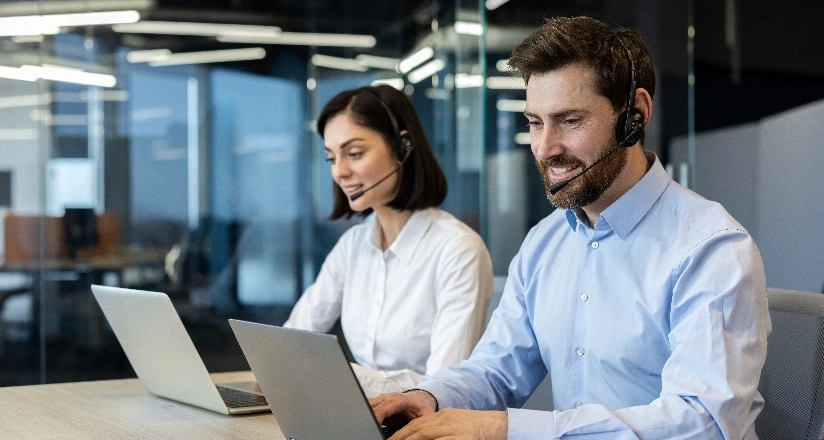 Two people with headsets are engaged in work on their laptops