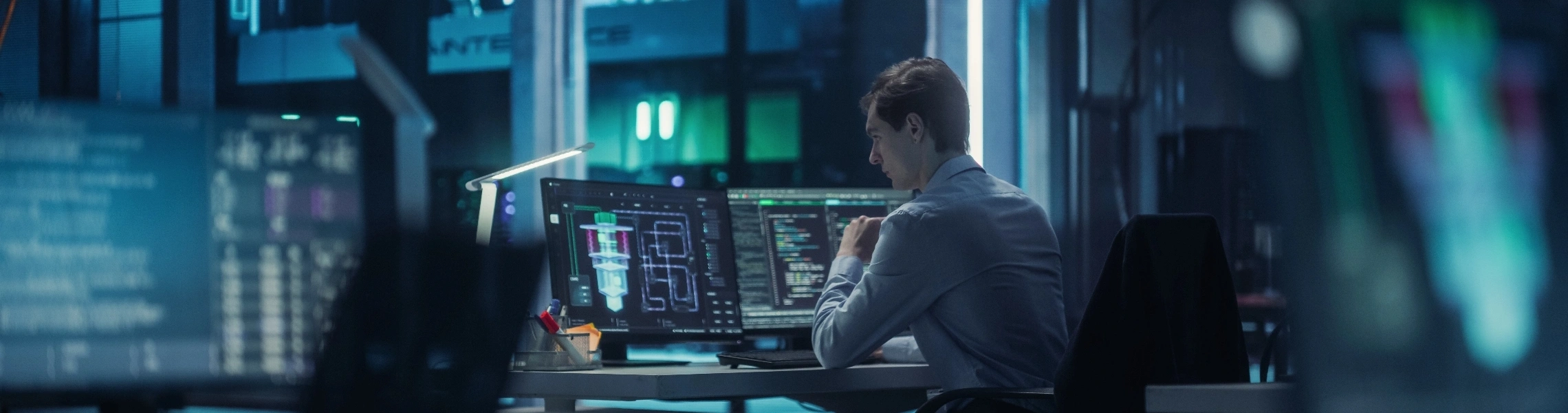 man seated at a desk, focused on multiple computer monitors displaying various applications and data